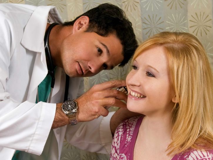 physician-conducting-an-examination-of-a-female-patients-left-ear-using-an-otoscope-725x544